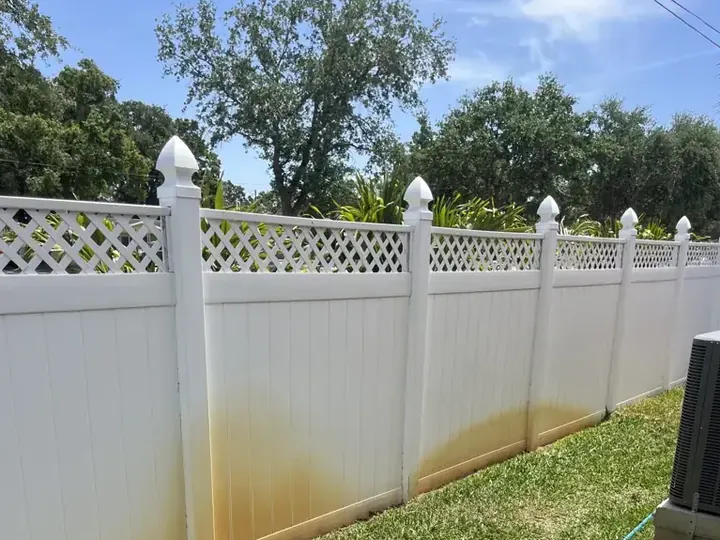 Lattice-top vinyl fence stained orange along the bottom, before rust removal