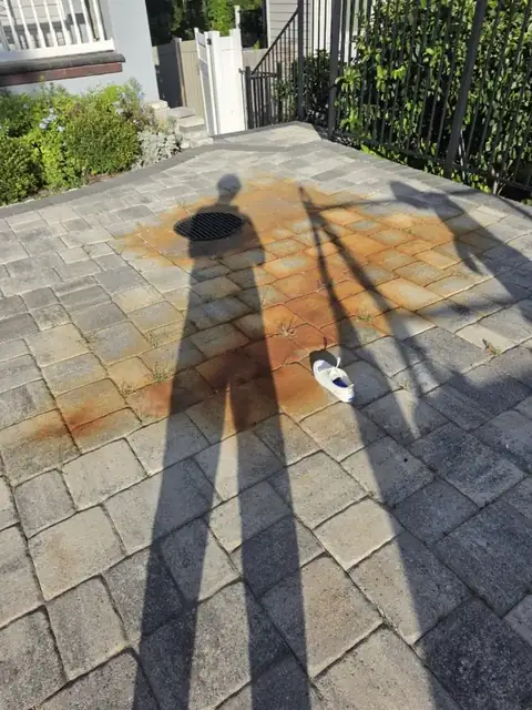 Gray paver patio with a large orange irrigation rust stain around a drain, before
