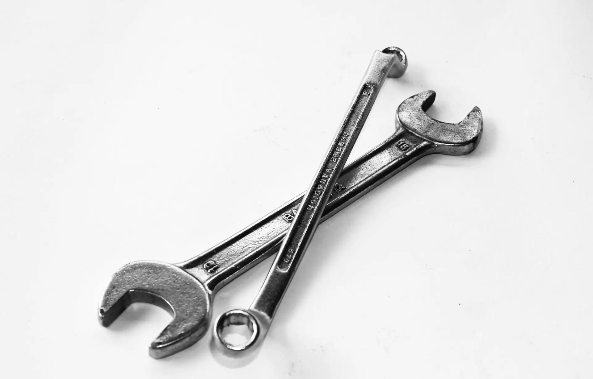 A pair of crossed metal wrenches on a clean white surface.