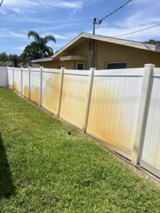 White vinyl fence with orange sprinkler rust stains before professional cleaning